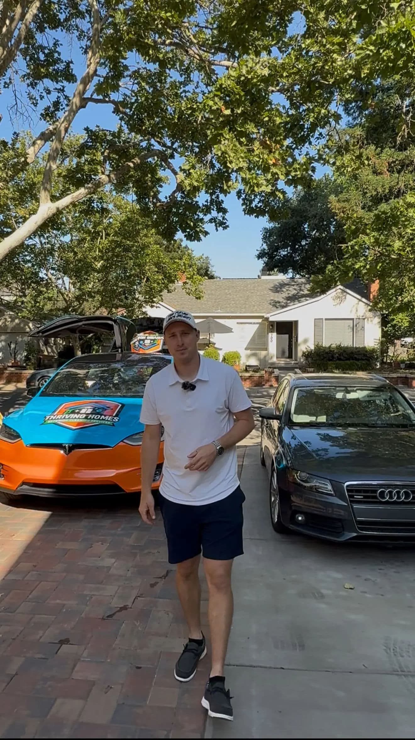 Man standing in driveway with vibrant orange and blue race car and a black Audi.