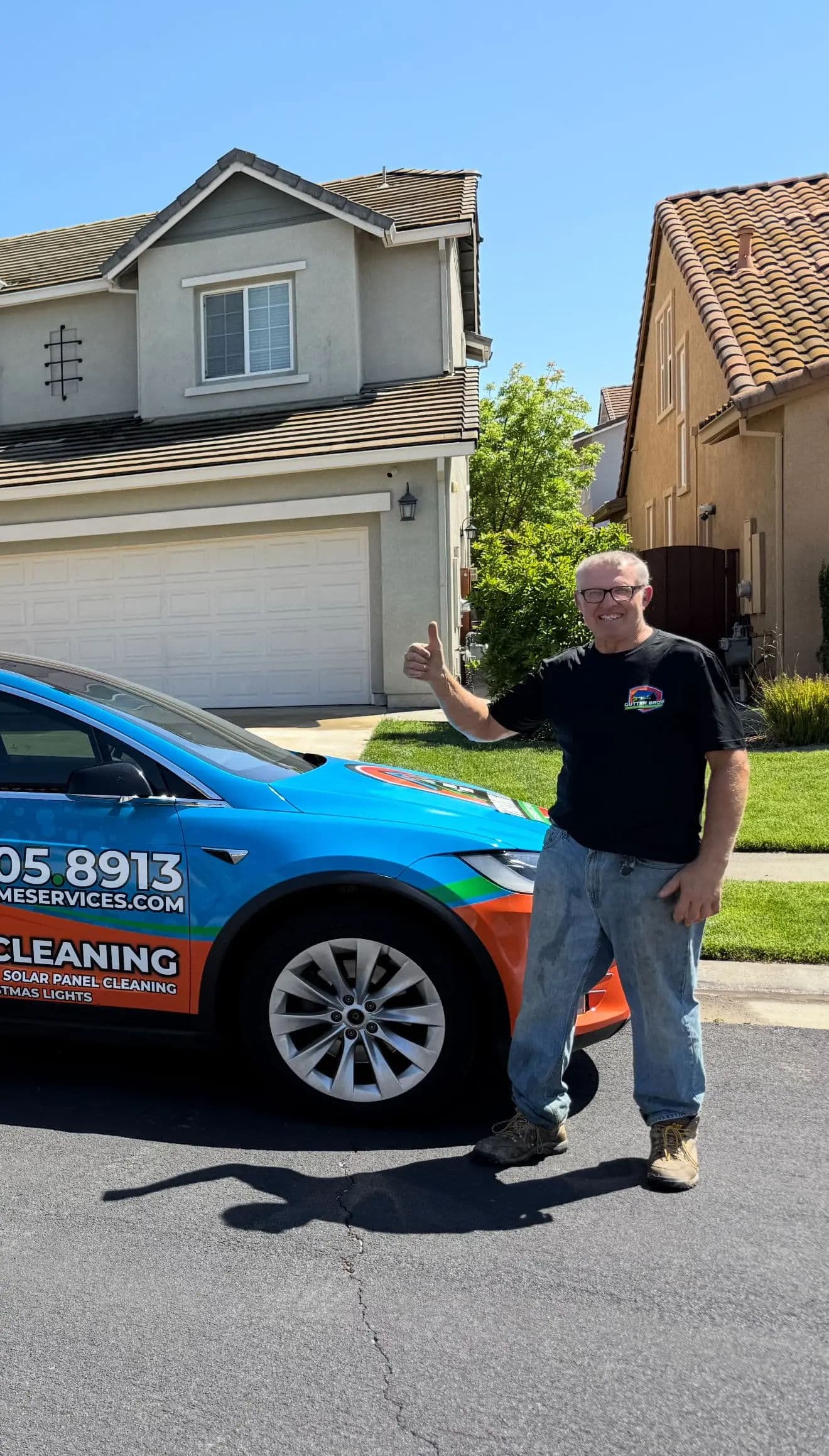 Man giving a thumbs up next to a blue car with solar panel cleaning service branding.